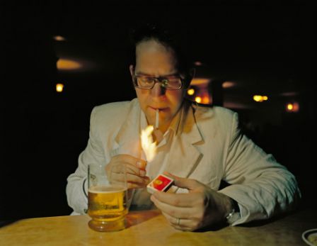 Man in white suit lighting cigarette in dark bar, India
